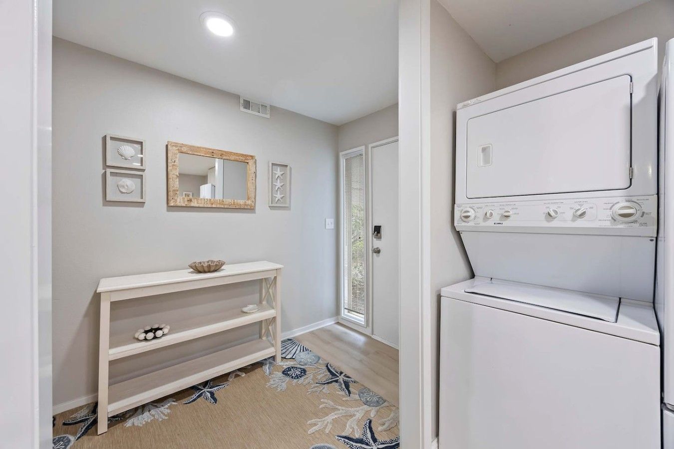 A laundry room with a built-in washer and dryer, a console table with decorative items, and a mirror on the wall.