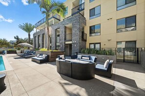 A modern outdoor lounge area with a pool, seating, and a stone facade building. - Game on! Just Remodeled! Luxurious Resort-Style 2B (San Diego)