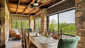 A rustic wooden dining area with stone walls, large windows, and a view of greenery. - Lake Views • 4 Kings • Hot Tub • Game Room (Forsyth)