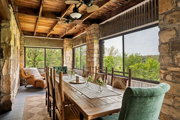 A rustic wooden dining area with stone walls, large windows, and a view of greenery.