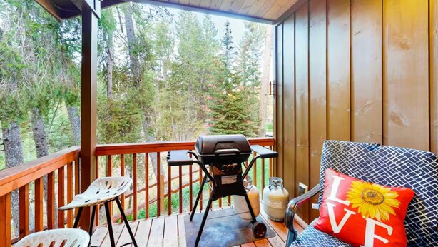 A covered deck with a grill, a chair, and a sofa with a 'LOVE' pillow. - Peaceful Wallowa Lake Cabin Near State Park (Joseph)