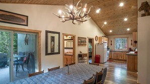 A dining area with a large table and chairs, a chandelier, and wooden flooring. - Peaceful Wallowa Lake Cabin Near State Park (Joseph)