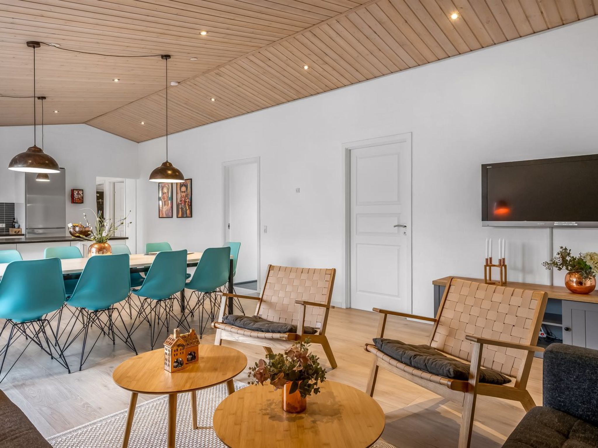 Un salon moderne avec un plafond en bois, un téléviseur à écran plat, des fauteuils de couleur turquoise et une table basse.