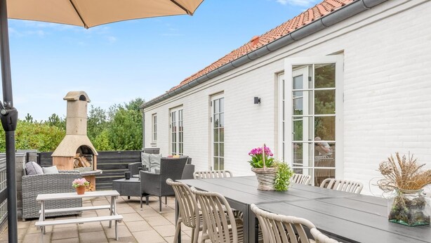 Une terrasse extérieure équipée d’une table à manger, de chaises, d’un barbecue et d’un grand parasol.
