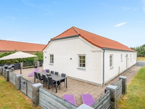A white building with a red-tiled roof, a patio with outdoor furniture, and a fenced area.