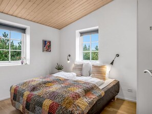 Une chambre avec un grand lit, deux fenêtres, un ventilateur de plafond et un tableau au mur.
