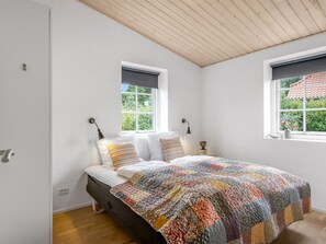 A bedroom with a bed, two windows, a wooden ceiling, and a view of greenery outside. - "Marjatta" - 3.2km from the sea by Interhome (Blåvand)