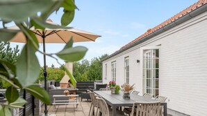 Une terrasse avec une table et des chaises, un barbecue et un bâtiment blanc en arrière-plan.