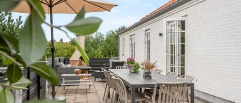 An outdoor patio with a dining table and chairs, a barbecue grill, and a large umbrella.
