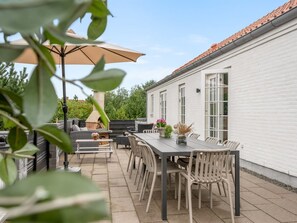 A patio with a table and chairs, a barbecue grill, and a white building in the background. - "Marjatta" - 3.2km from the sea by Interhome (Blåvand)