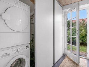 A laundry room with stacked washing machines and a door leading to a balcony with a view of greenery.
