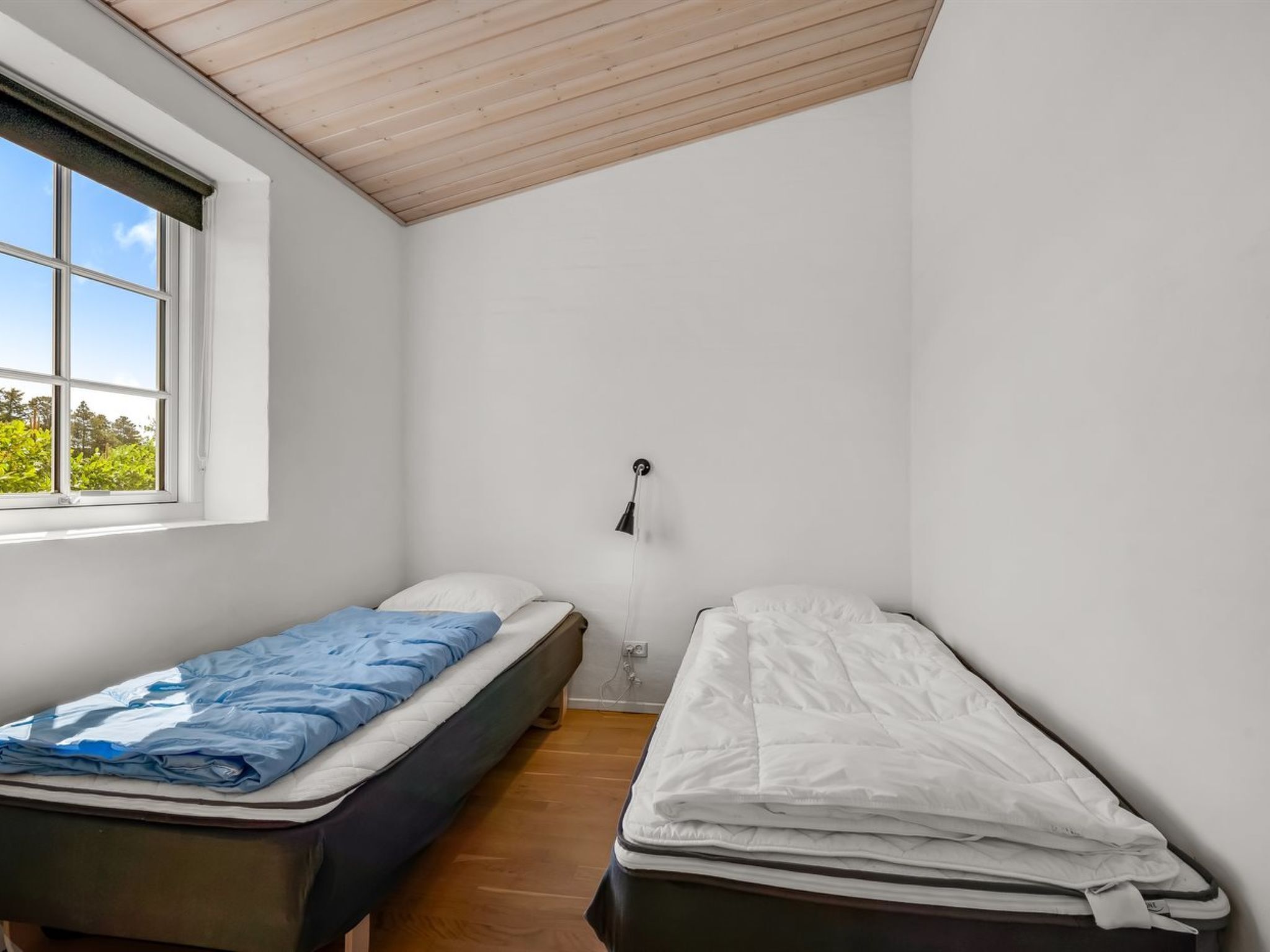 Ein kleiner, einfach eingerichteter Raum mit zwei Einzelbetten, einem Fenster mit Blick auf Grünflächen und einer Holzzielende.