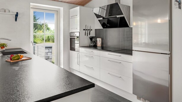 A modern kitchen with white cabinets, a black countertop, stainless steel appliances, and a wooden ceiling. - "Sod" - 3.2km from the sea by Interhome (Blåvand)