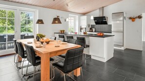A modern kitchen with a wooden ceiling, a dining area with a wooden table and black chairs, and a large window providing a view of greenery. - "Sod" - 3.2km from the sea by Interhome (Blåvand)