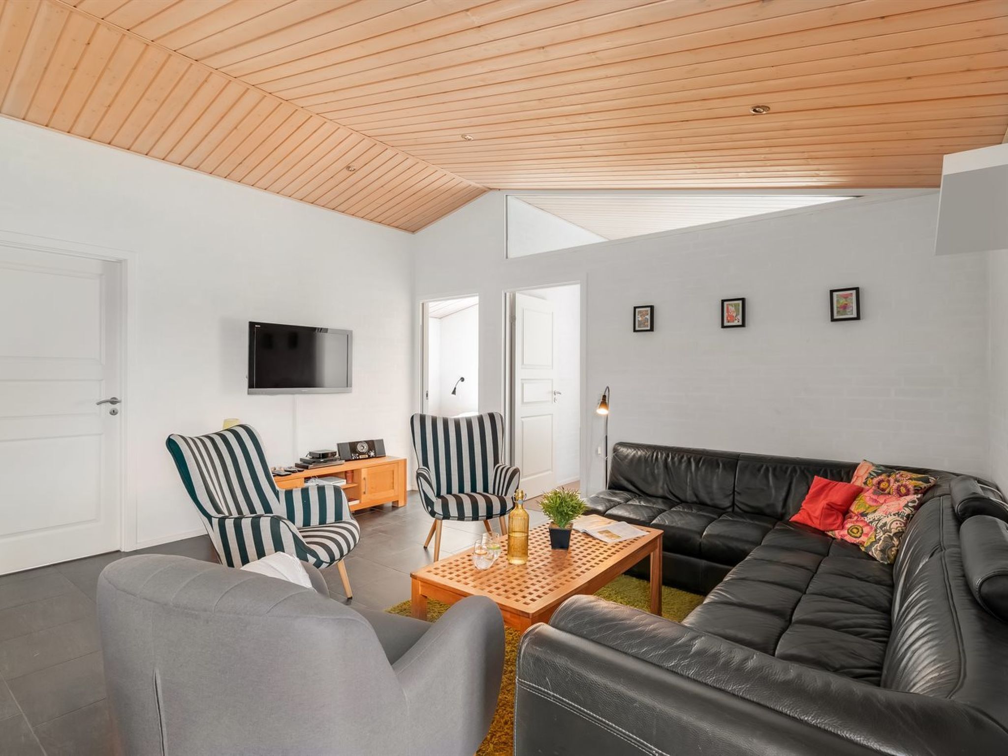 Una sala de estar moderna con un sofá de cuero negro, sillones a rayas, una mesa de centro de madera y un televisor de pantalla plana montado en la pared.