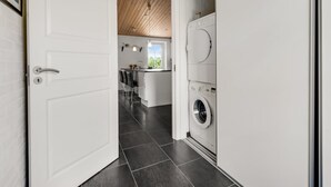 A modern kitchen with a built-in washer and dryer, a wooden ceiling, and a view of the backyard. - "Sod" - 3.2km from the sea by Interhome (Blåvand)