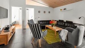 A modern living room with a wooden ceiling, a black leather sofa, a striped armchair, a grey armchair, a wooden coffee table, and a TV mounted on the wall. - "Sod" - 3.2km from the sea by Interhome (Blåvand)