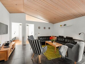 Ein modernes Wohnzimmer mit Holzboden, einem schwarzen Ledersofa, einem gestreiften Sessel, einem grauen Sessel, einem Holztisch und einem flachen Fernseher, der an der Wand befestigt ist.