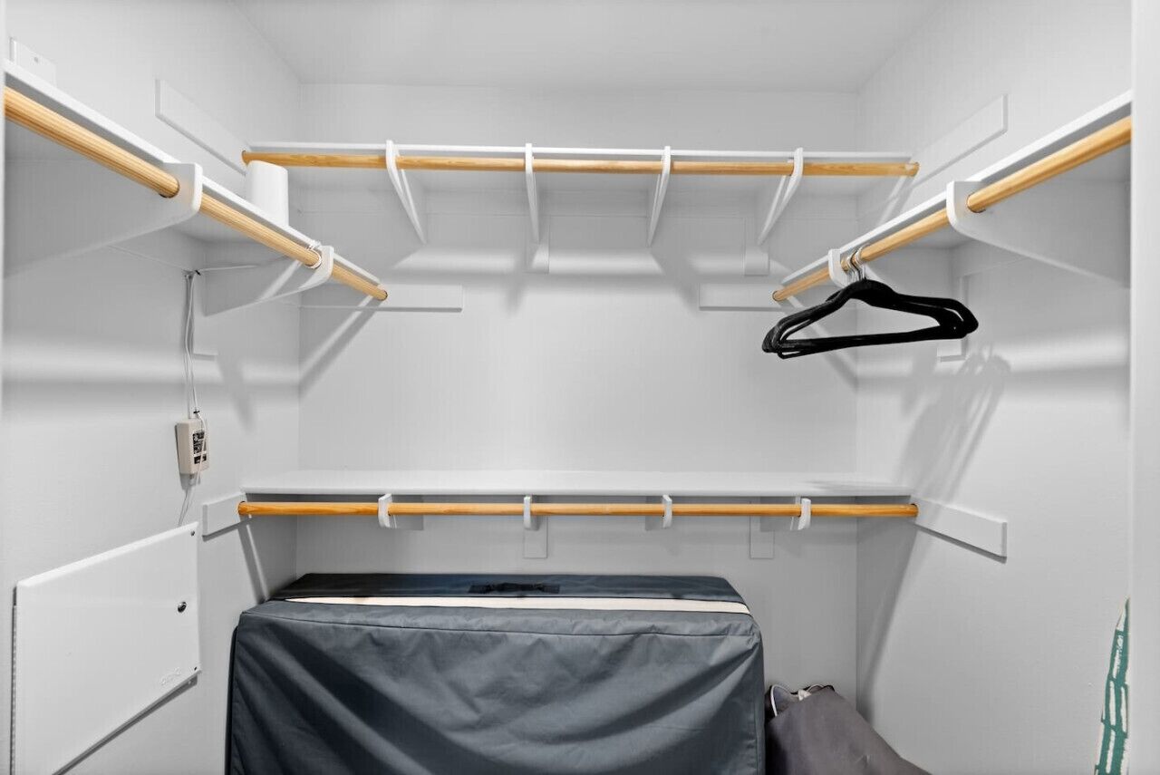 A compact room with a built-in wardrobe featuring multiple wooden shelves and a hanging rod.