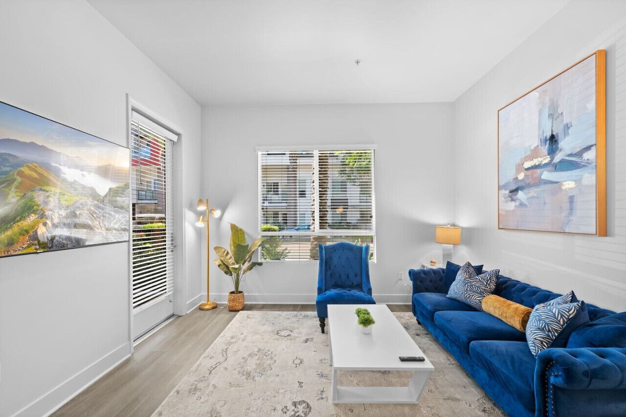 A modern living room with a blue sofa, white coffee table, and a large painting on the wall.