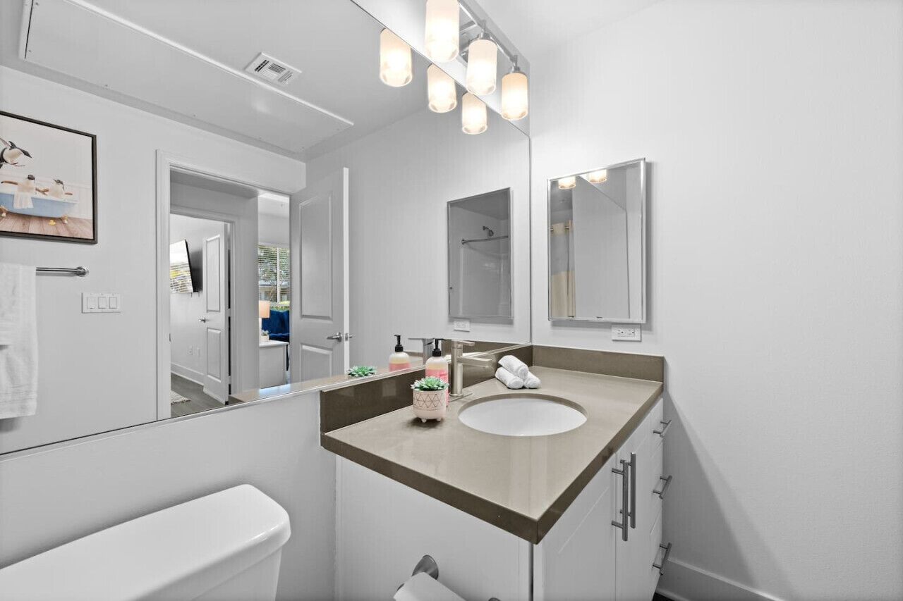 A modern bathroom with a white toilet, a beige sink, and a large mirror.