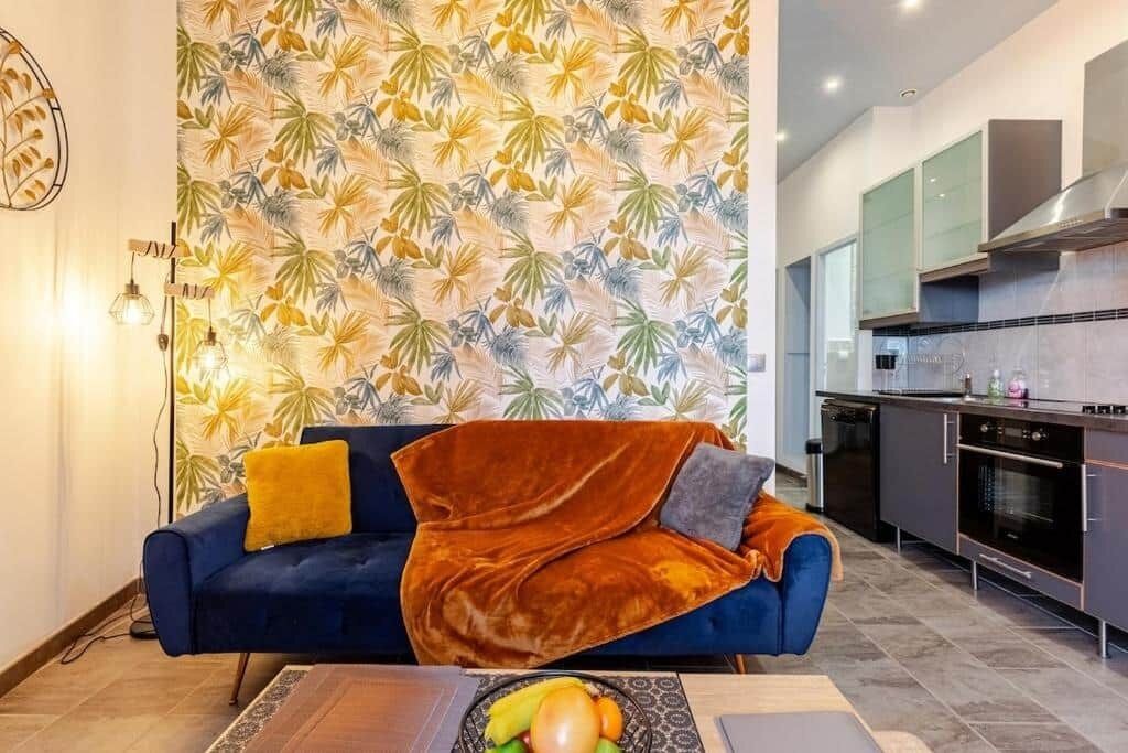 Un soggiorno moderno con un divano blu, una parete decorata e una cucina sullo sfondo.