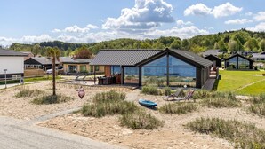 A modern house with large glass windows, a patio with lounge chairs, and a view of the surrounding landscape. - "Catalina" - 30m from the sea by Interhome (Sjølund)