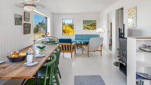 Eine moderne Küche mit Einbauherd, ein Essbereich mit Holztisch und grünen Stühlen sowie ein blaues Sofa.