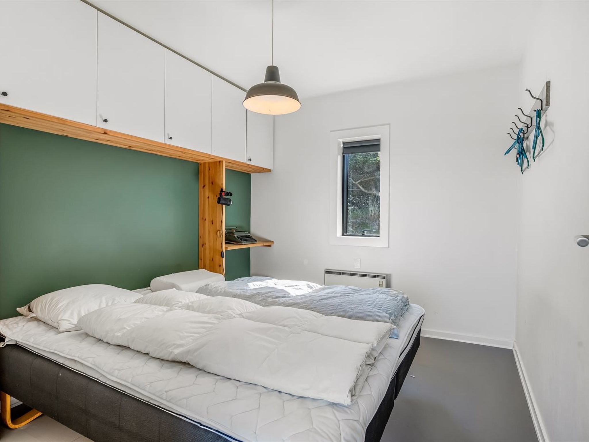 A modern bedroom with a bed, a wooden shelf, a window, and a hanging light fixture.
