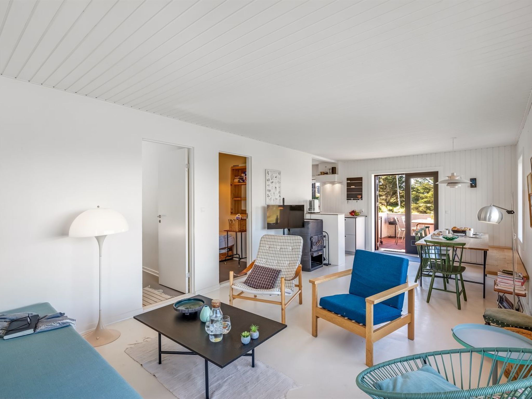 A spacious living area with a sofa, chairs, a table, and a kitchen in the background.