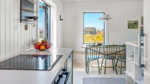 Eine moderne Küche mit großem Fenster, ein Essbereich mit grünen Stühlen und Blick auf einen roten Bauernhof und Felder.