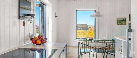 Eine moderne Küche mit großem Fenster, ein Essbereich mit grünen Stühlen und Blick auf einen roten Bauernhof und Felder.