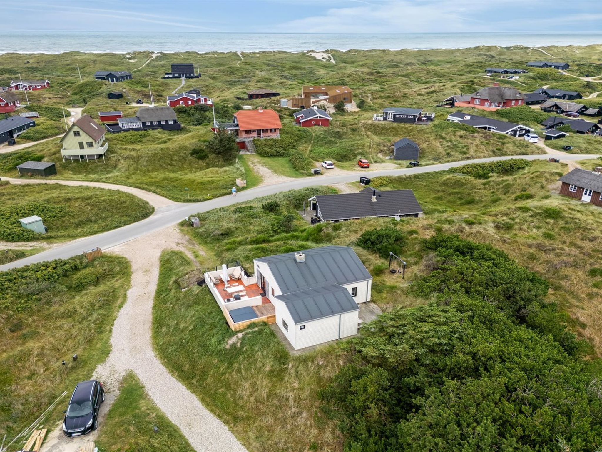 Vue aérienne d’un village côtier avec des maisons, un chemin de gravier et une voiture garée sur le bord de la route.