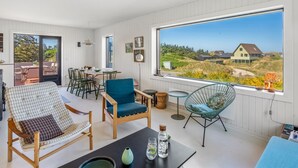 Ein modernes Interieur mit Essbereich, einer Sitzecke inklusive Sofa und Sesseln sowie einem großen Fenster mit Landschaftsblick.