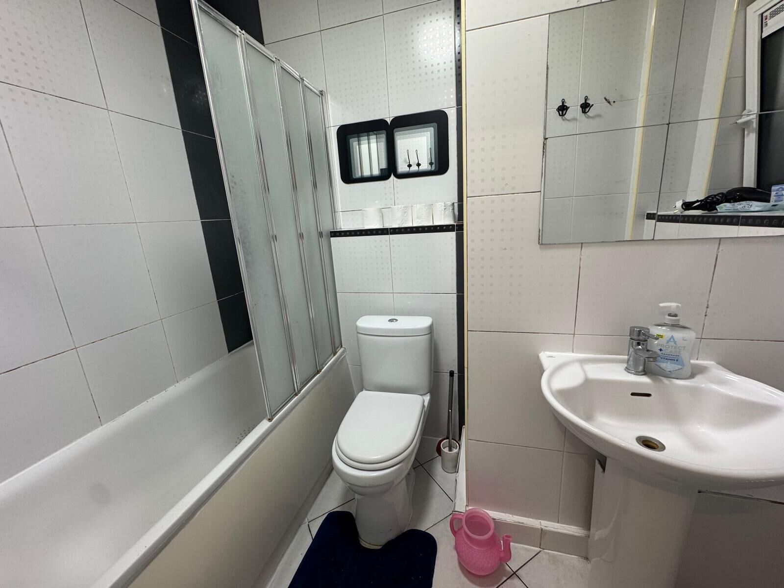 A bathroom with a toilet, a sink, a shower, and a mirror.