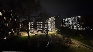 En nattbild av ett bostadsområde med upplysta hyreshus, en liten park och en lekplats.