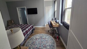 A bedroom with a bed, a desk with a globe, a chair, a lamp, a ceiling fan, and a window with blinds. - Highlands Hideaway - Walk to Bars, Food & Coffee (Louisville)