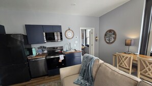 A compact living space with a kitchenette, a sofa, a dining table, and a lamp. - Highlands Hideaway - Walk to Bars, Food & Coffee (Louisville)