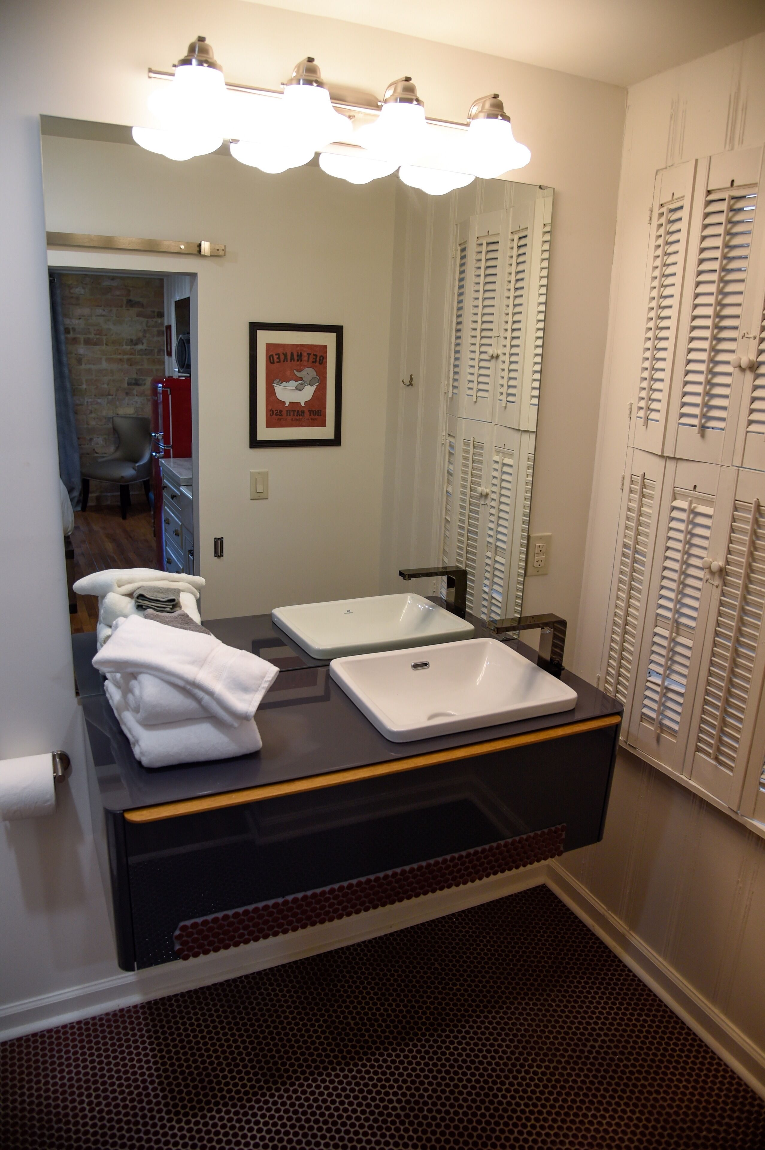 A bathroom with a vanity, two sinks, a mirror, and a shower area.