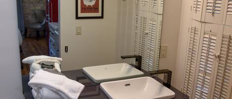 A bathroom with a vanity, two sinks, a mirror, and a shower area.