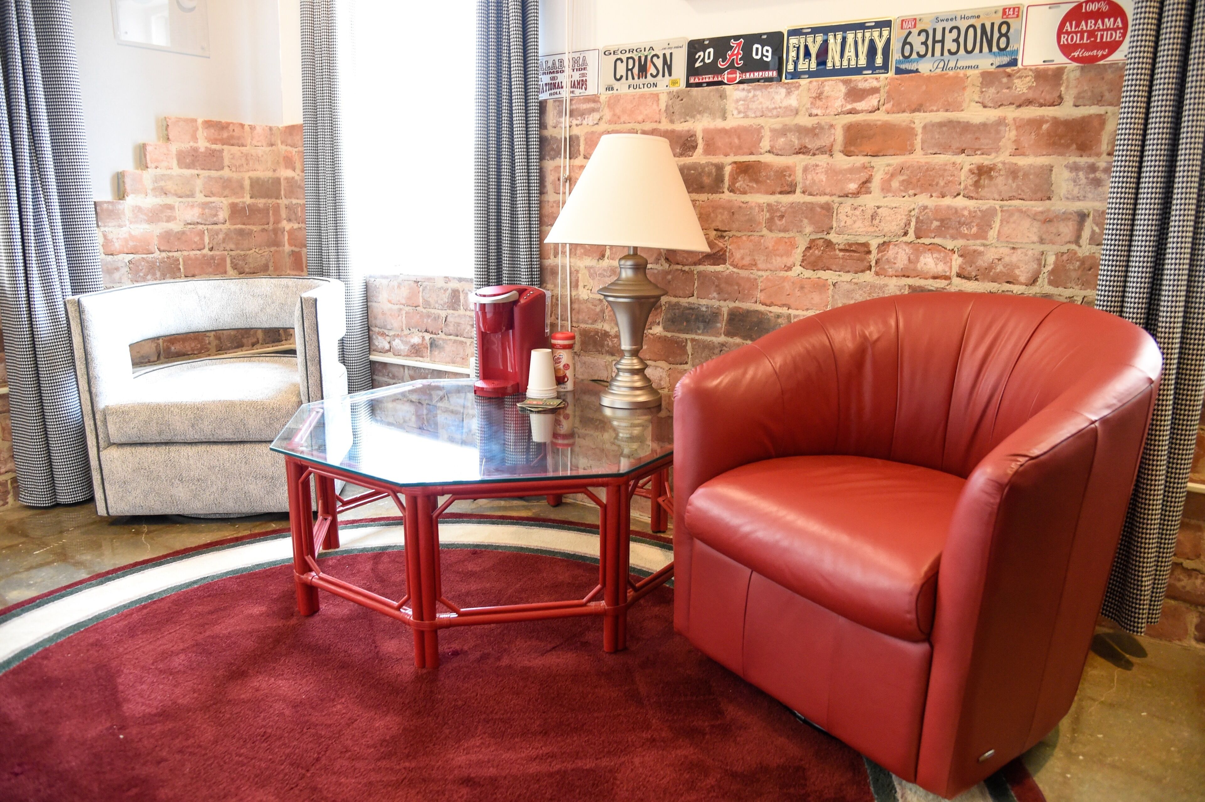 A room with a brick wall, a red leather chair, a glass table, and a lamp.