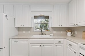 A kitchen with white cabinets, a dishwasher, a window with a view, and a countertop with a sink. - The Neptune House 3 bedrooms by the sea (St Simons Island)