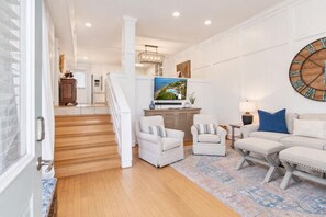 A modern living room with a staircase, a television, and a large wall clock. - The Neptune House 3 bedrooms by the sea (St Simons Island)