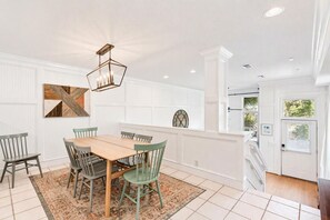 A dining area with a wooden table and chairs, a geometric wall art piece, and a ceiling light fixture. - The Neptune House 3 bedrooms by the sea (St Simons Island)