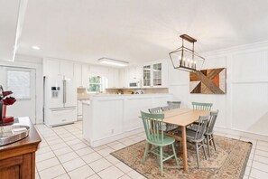 Une cuisine moderne avec des meubles blancs, un îlot central et un coin repas comprenant une table et des chaises en bois.