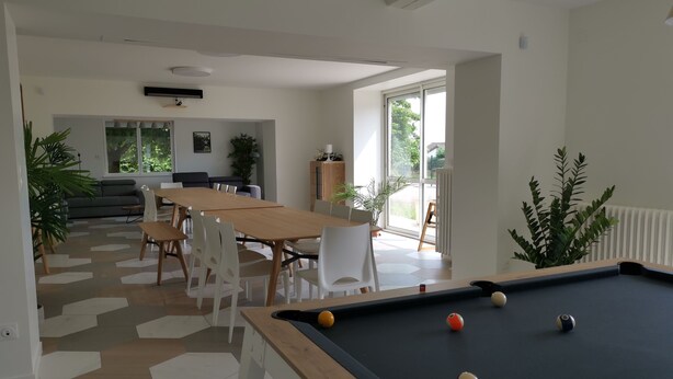 Uma sala de estar moderna com mesa de bilhar, área de jantar com uma mesa grande e cadeiras, e um sofá.