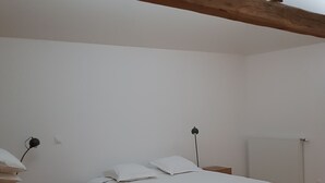 Quarto com cama, vigas de madeira, mesa de cabeceira, luminária e radiador.