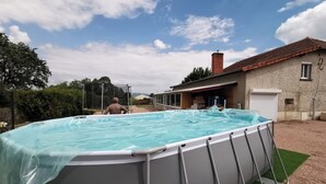 Piscina externa com deck coberto, casa com telhado de telhas vermelhas e garagem.