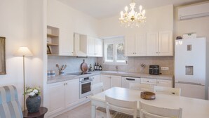 A modern kitchen with white cabinetry, a dining table, and a chandelier. - Casa Pino-private family villa with pool in Corfu, close to beaches/water park (Corfu)