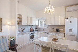 A modern kitchen with white cabinetry, a dining table, and a chandelier. - Casa Pino-private family villa with pool in Corfu, close to beaches/water park (Corfu)